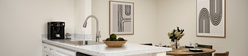 A kitchen with a white countertop and a dining table with chairs.