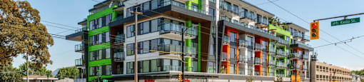 A street view of a multi-story building with a green and orange facade at 388 Kaslo East Village Apartments.