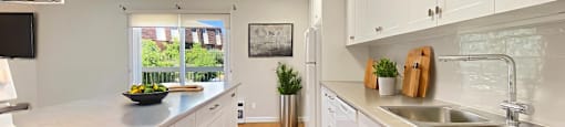 A modern, partially-open, galley style kitchen with white cabinets and a grey countertop at Moira Apartments in Belleville, ON
