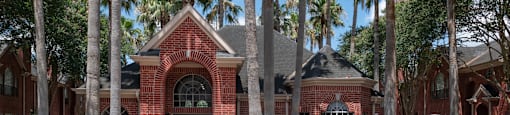 A red brick building with a black door and windows surrounded by palm trees.