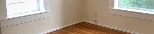 an empty room with a wooden floor and two windows