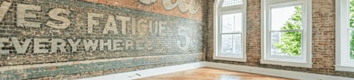 an old mural on a brick wall in an empty room with hardwood floors and a ceiling