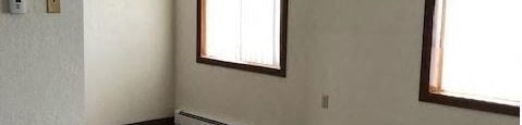 an empty room with a wood floor and a window at Woodridge Apartments, Kenai, Alaska
