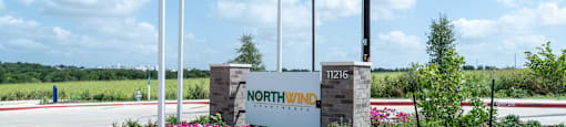 A sign for Northwind stands in front of a road with a flagpole and flowers.