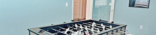 A foosball table is in a room with a blue wall and a sign that says "Come to Play".
