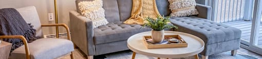 A living room with a grey couch, a wooden chair, a round coffee table, and a floor lamp.