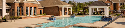 Dog-Friendly Apartments in Richmond, VA - Clairmont at Chesterfield - Resort-Style Swimming Pool With Bubbling Hot Tub, Wide Sundeck, Clubhouse Building, and Covered Pavilion Under Blue Sky.