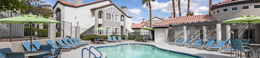 A swimming pool surrounded by lounge chairs and umbrellas with a building in the background.