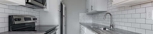A kitchen with white cabinets and a black and white tiled backsplash.
