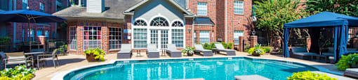 A pool surrounded by lounge chairs in front of the leasing office at The Inverness Apartments in Houston, TX