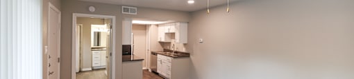 View from living area into kitchen and bedroom. Ceiling fan in living area, whit cabinets and stainless appliances in kitchen