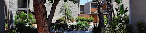 View of exterior buildings and side walk winding in between with lush landscaping and trees