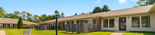 Building exterior of Fairington Apartments in Anderson, featuring windows, and patios, with a sidewalk in front, a lawn, and a bench.