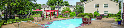 A swimming pool surrounded by a concrete patio and a red umbrella.