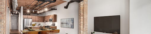 Open-concept loft at Lofts at River East with exposed brick, high timber ceilings, dining area, and living room flowing into the kitchen.