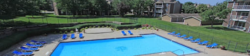 Huge swimming pool with spacious sundeck, poolside lounge chairs, beautiful landscaping, scenic views, lots of trees at LionsGate Apartments in Lincoln, Nebraska