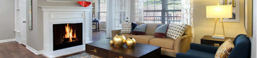 Living room with wood plank floors, gray wall color, wood burning fireplace, oversized window, and built-in shelves.