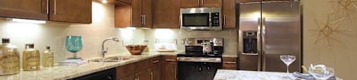 Luxury apartments with spacious kitchen and built-in wine rack, granite countertops, kitchen island, stainless steel appliances, and designer tile backsplash at Tuscany Walk Apartments in Houston Texas.