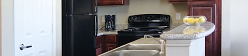 A kitchen with a black refrigerator and brown cabinets.