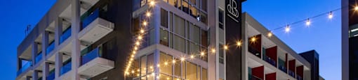 A modern building with a combination of white and red sections is illuminated with string lights.