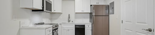 A kitchen with white cabinets and appliances, a wooden floor, and a door on the right.