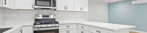 A kitchen with white cabinets and a stainless steel stove top oven.