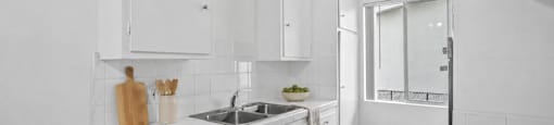 A white kitchen with a wooden cutting board and utensils on the counter.