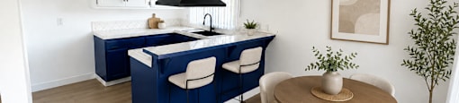 A kitchen with a blue island and white chairs.
