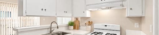 A white kitchen with a sink, stove, and cabinets.