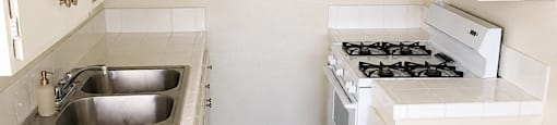 A white kitchen with a stove, sink, and cabinets.