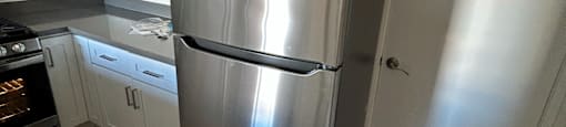 A stainless steel refrigerator in a kitchen with wooden flooring.