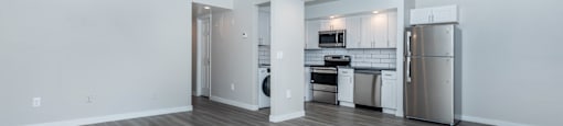 an empty living room with a kitchen and a ceiling fan