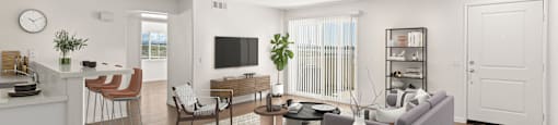 A modern living room with a grey sofa, wooden floors, and a white kitchen area.