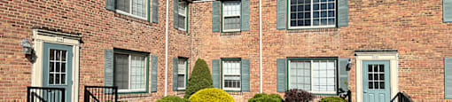 A brick building with green shutters and bushes in front.