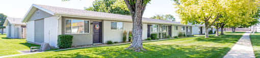 a row of houses in a yard with grass and trees at Cadence Apartments, Roy