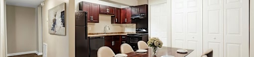 A dining room with a table set for two and a kitchen in the background.