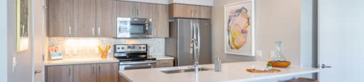 Three-Bedroom apartments in Tigard, OR - Sygnii - Kitchen with Stainless Steel Appliances, Wood-Grain Cabinetry, and Peninsula with Three Bar Stools.
