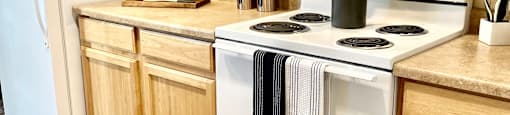 Spokane, WA Apartments for Rent - Deer Creek - Kitchen with Plank Flooring, Rug, White Appliances, and Wood-Tone Cabinetry.