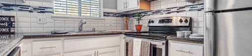 Townhouses for Rent in San Jose, CA - Los Gatos Creek - Kitchen Featuring White Cabinetry, Tile Backsplash, Dark Countertops, Stainless Steel Appliances, and a Window with Blinds.