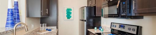 Apartments In League City For Rent - Anchor At South Shore - Kitchen With Cabinetry, Faux Wood Flooring, Granite Countertops, A Double Stainless Steel Sink, And Stainless Steel Appliances.
