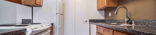 Studio Apartments in San Jose, CA - Village of Taxco - Kitchen with Wood-Style Flooring, Double Sink, White Appliances, Wood-Style Cabinets, and Granite Countertops and Dishwasher.