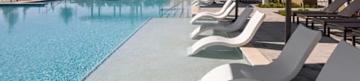 A pool with white chairs and a shade structure at Boardwalk at Research Park apartments in Huntsville, AL.