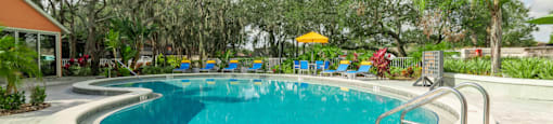 a resort style pool with lounge chairs and trees in the background