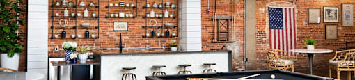 A pool table is in the middle of a room with a brick wall and a bar area.