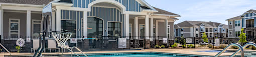A swimming pool in front of a house with a basketball hoop.