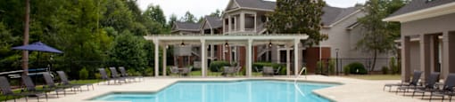 Resort-style swimming pool at 1287 Shoals Apartments in Athens, GA, surrounded by lounge chairs, lush greenery, and modern residential buildings in the background.