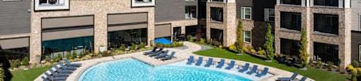 A large swimming pool surrounded by lounge chairs in front of apartment buildings at Liam at Hays Farm in Huntsville, Alabama
