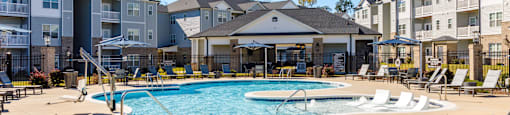 A pool surrounded by lounge chairs in front of apartment buildings.