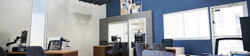 A room with blue walls and wooden floors has several chairs and desks arranged in it.