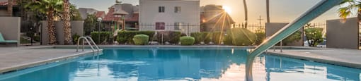 Sparkling pool with handrail, apartments, palm trees and sunset in background